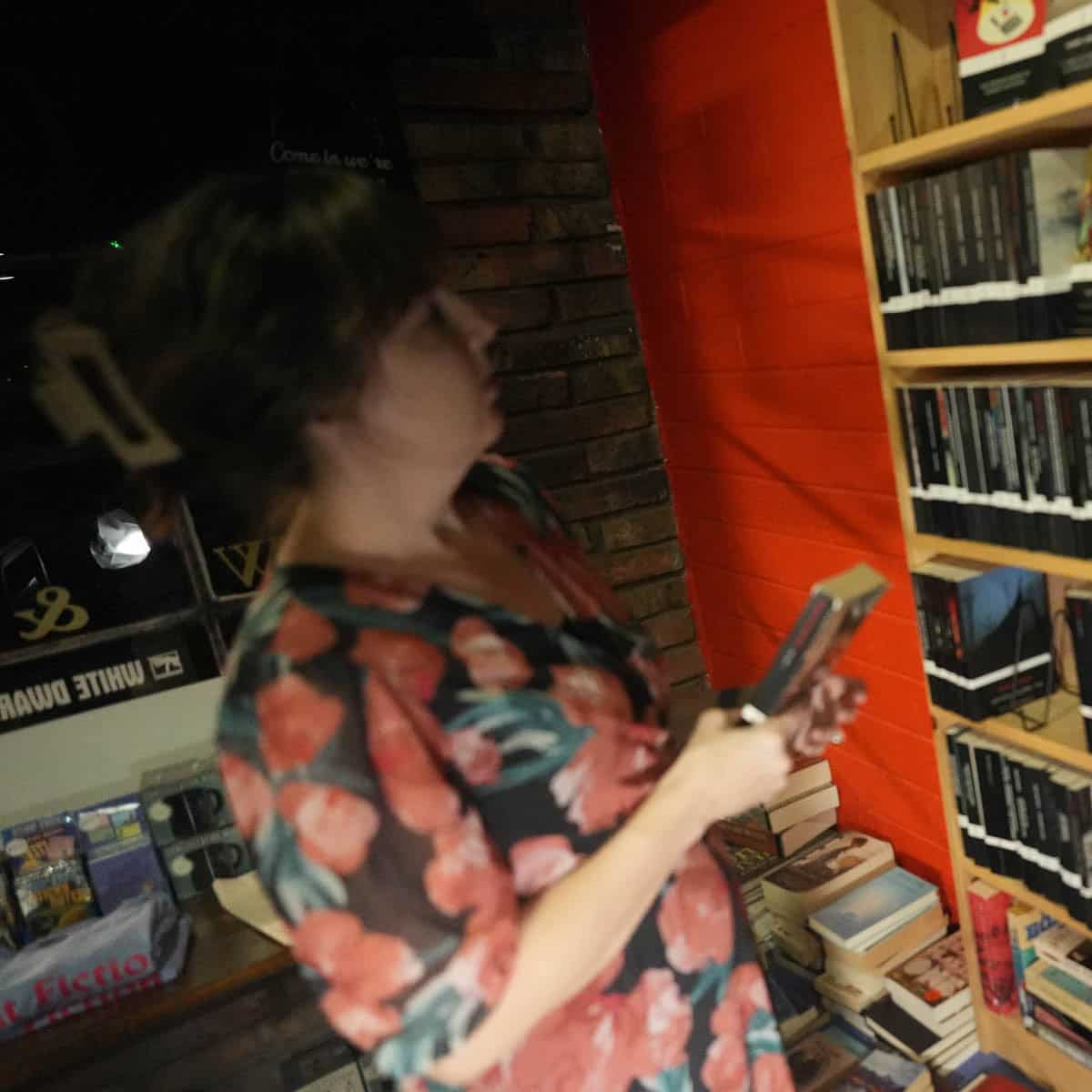 Woman browsing books in Cult Fiction Bookshop with shelves and warm lighting.
