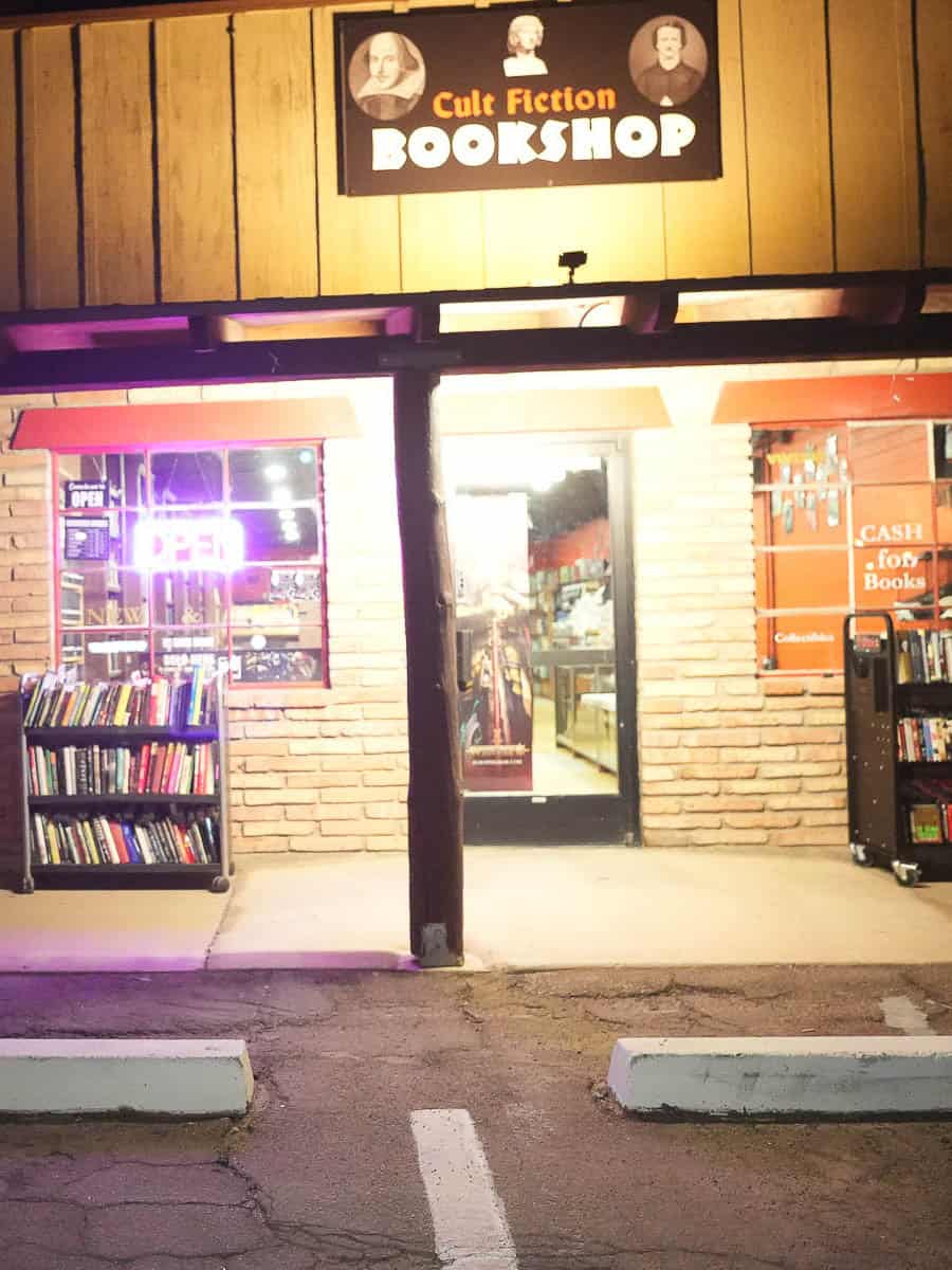 Exterior view of Cult Fiction Bookshop with neon sign and bookshelves.